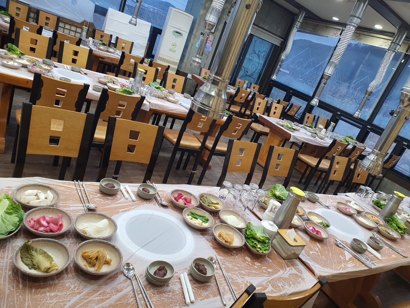 만복래숯불구이 매장. 창밖 산이 보이는 홀에 밑반찬이 차려진 테이블.